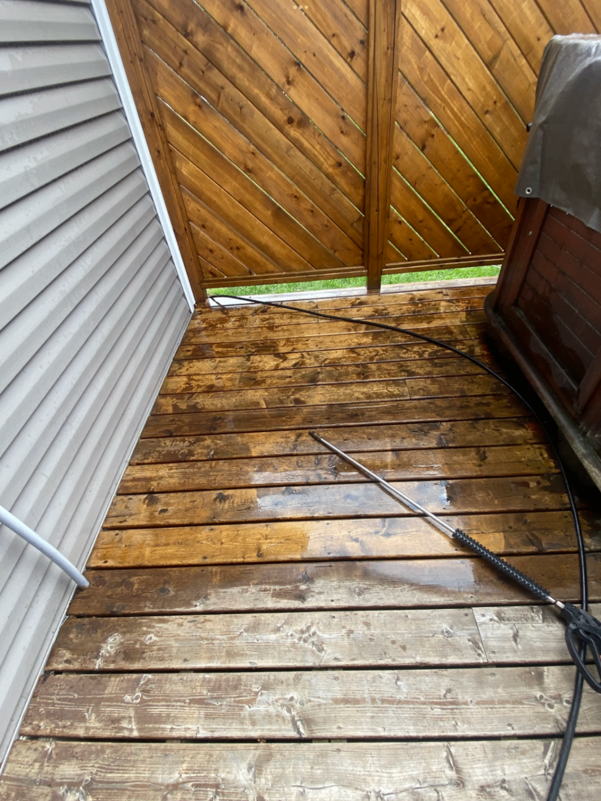 Deck corner before cleaning with weathered wood and pressure washer wand visible